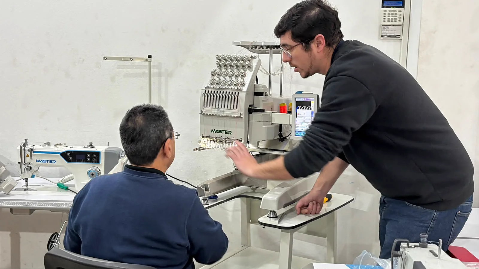 Dos técnicos de Casa Vargas reparando una bordadora industrial Master en el taller